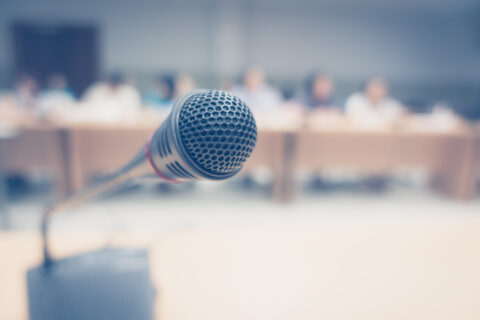 Black microphone in foreground with people sitting at meeting in soft focus background